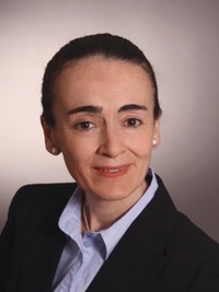 Professional headshot of a woman with dark hair, wearing a black blazer and light blue shirt.